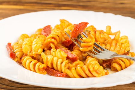 Italian pasta fusilli with tomato sauce and sausage skewered on fork in plate, close-up, selective focus.の写真素材