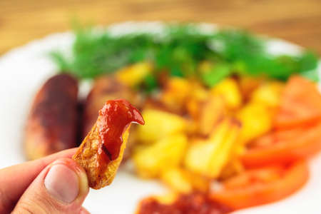 Hand holding piece of fried potato with ketchup, selective focus, blurred backgroundの写真素材