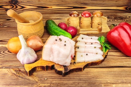 Piece and sliced fresh, raw pork lard on wooden board with vegetables, spices on the table