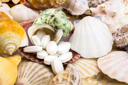 Calcium natural food supplement pills on the beautiful, mixed seashells backgroundの写真素材