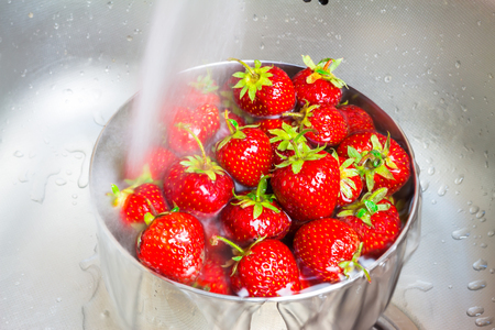 Bowl of organic strawberry in the sink under running water.の写真素材