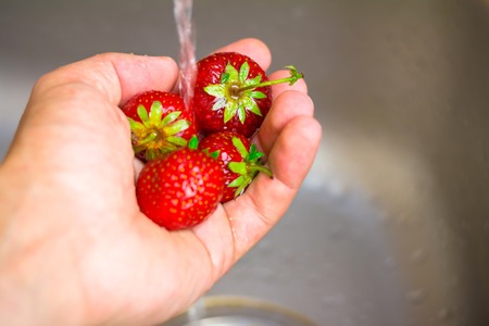 Ripe, organic strawberry in the hand under running water on kitchenの写真素材