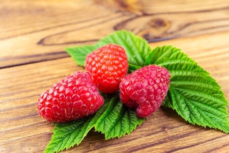 Fresh, ripe raspberries on leaves, rustic wooden background