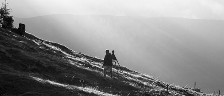 Photographer with camera on tripod in mountains under sun rays, black and white photoの写真素材