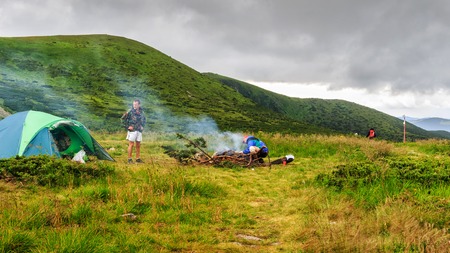 Camping tent and two men tourists at campfire in Carpathian mountains, summertime journey