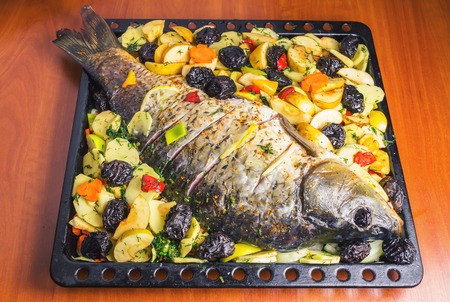 Carp fish prepared for cooking in baking dish with vegetablesの写真素材
