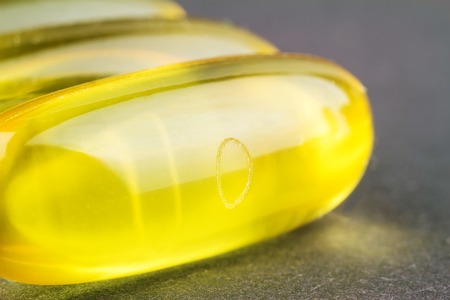 Natural food supplement, yellow gel pill, fatty acid omega 3 capsules, fish oil, on black background, macro imageの写真素材