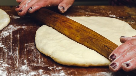 Rolling pin in hands, rolling dough on the wooden table, close-up