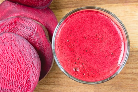 Fresh beet juice in glass and sliced beetroot on wooden table, top view