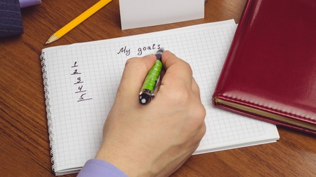 Man writes goals text on the page of notepad on the table. concept of planning success future
