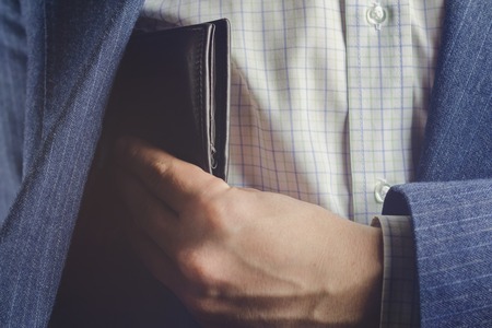 Business man pulls out or put his leather wallet into jacket pocketの写真素材