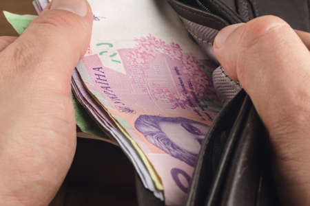 Close-up view of male hands opened the wallet with ukrainian money currency hryvnia on wooden...