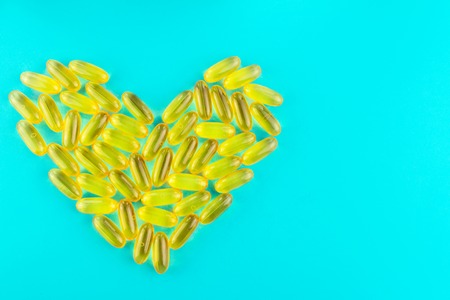 Lot of yellow capsules omega 3, fatty acid, fish oil in heart shape on blue background
