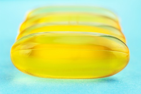 Yellow capsules of omega 3, fatty acid, fish oil on blue background, macro imageの写真素材