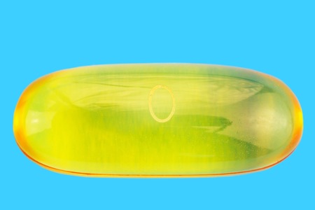 One yellow capsule of omega 3, fatty acid, fish oil on blue background, macro imageの写真素材