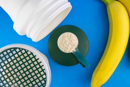 Protein powder in the measuring plastic spoon, shaker bottle with milk and two banana on blue background, sports nutrition after training, top view.の写真素材