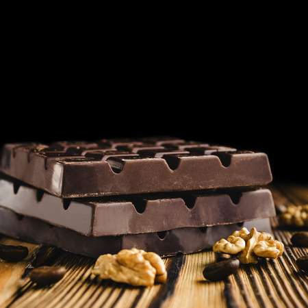 Three pieces of bitter, dark chocolate bar, walnut core and coffee bean on wooden background, close-up view.の写真素材