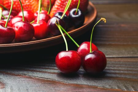 Fresh organic cherries on dark wooden planks and full plate with berries on the background, close-up, selective focus.の写真素材