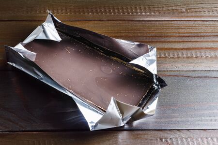 Bitter, dark chocolate bar in foil on wooden background.の写真素材