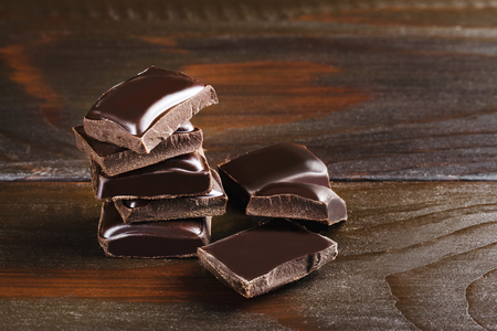 Pieces of bitter, dark chocolate, cubes on heap at wooden background, close-up view.の写真素材
