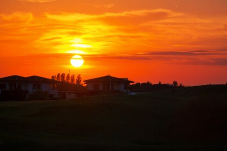 Red and orange sunset sky with big sun above the houses in dusk, sunset scenery.の写真素材