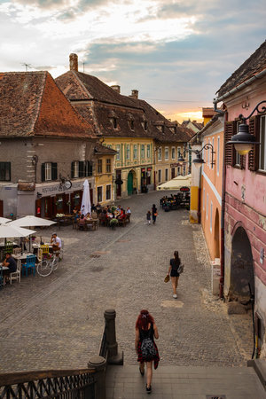 SIBIU, ROMANIA - JUNE 19, 2017: View on the medieval street with ancient houses, outdoors cafe and people at the sunset time.のeditorial素材