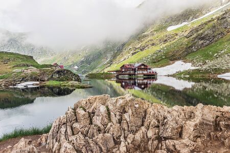 Nature landscape of amazing glacier lake Balea with house on shore and Fagaras mountains with white...
