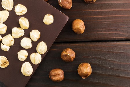 Part of bitter dark chocolate bar with hazelnut on wooden planks background, top view.の写真素材