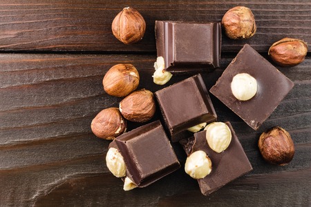 Pieces of bitter dark chocolate cubes with hazelnut on wooden planks background, top view.の写真素材