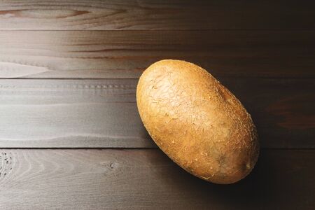 Uncooked, fresh whole one potato on wooden table of dark brown planks background, close-up view.の写真素材