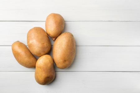 Uncooked, fresh crop of potatoes on wooden table of white planks background, top view.の写真素材