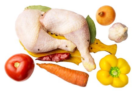 Two raw chicken legs at cutting board with spices and vegetables such as tomato, carrot, pepper, garlic, red chili pepper, onion isolated on white, top view.の写真素材