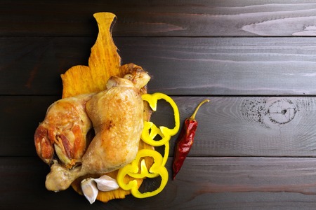 Two roasted chicken legs on cutting board with vegetables and spices at dark wooden planks, top view.の写真素材