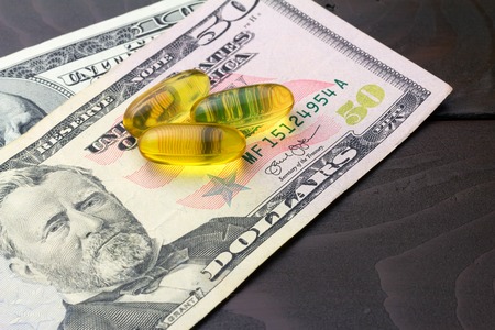 Yellow capsules omega 3, fatty acid, fish oil on dollar banknote at wooden table.の写真素材