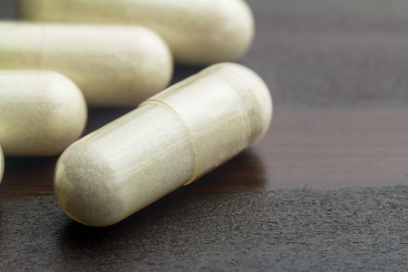 White capsules of glucosamine chondroitin, healthy supplement pills on wooden table, macro image.