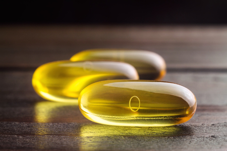 Yellow capsules omega 3, fatty acid, fish oil on dark wooden table, macro image.の写真素材