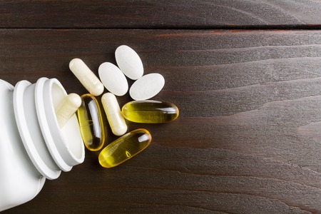 Complex of vitamins and dietary supplement, yellow capsules omega 3, white of glucosamine, calcium pills, white plastic bottle on wooden table, top view.の写真素材