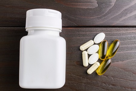 Complex of vitamins and dietary supplement, yellow capsules omega 3, white of glucosamine, calcium pills, white plastic bottle on wooden table, top view.の写真素材