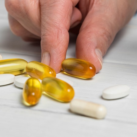 Woman hands takes yellow capsules of omega 3, white pills of calcium, glucosamine supplements on...
