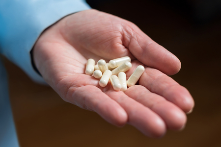 White medication capsules of glucosamine, healthy supplement pills in woman palm hand.