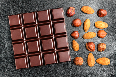 Dark, bitter chocolate bar, almond and hazelnut on black leather texture background, top view.の写真素材