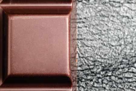 Dark, bitter chocolate in cubes shape on black leather texture background, top view.