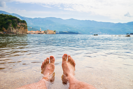 Two hairy man legs in the transparent Adriatic sea water on Mogren beach, view to the old city Budva.の写真素材