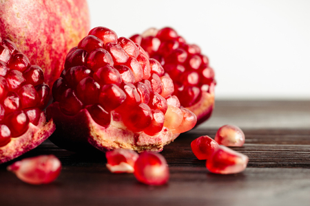 Pomegranate seeds and whole fruits on the dark brown wooden planks and white background, close-up view.の写真素材