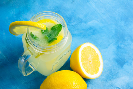 Refreshing lemonade drink with lemon slice and mint in the jar on a blue background.の写真素材