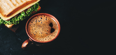 Cup with hot coffee and sandwich with grilled toast, salami sausage, salad lettuce and cheese on a dark background.の写真素材