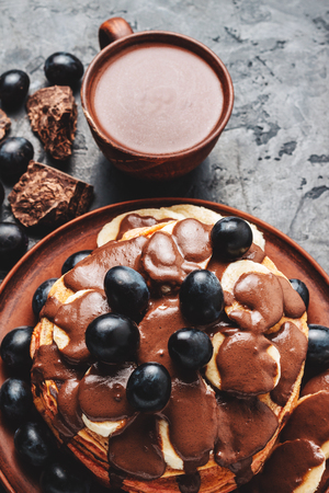Pancakes with banana, chocolate sauce and grapes in a plate and hot chocolate drink in a cup on dark background.の写真素材
