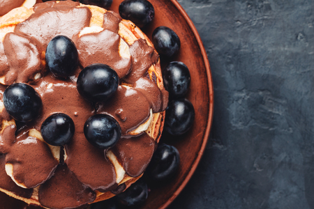Pancakes with banana, chocolate sauce and grapes in plate, on dark background, top view.の写真素材
