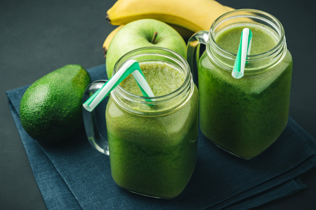 Green, healthy, detox smoothie from avocado, banana, apple in mason jar on blue napkin, dark background, vegetarian food.の写真素材