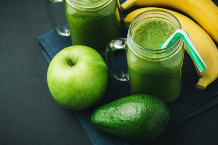 Green, healthy, detox smoothie from avocado, banana, apple in mason jar on blue napkin, dark background, vegetarian food.の写真素材